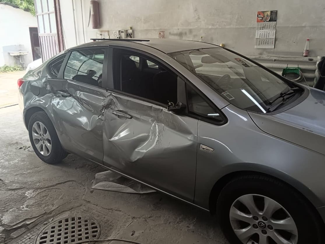 Opel Astra sedan gri cu ambele uși de pe o parte înfundate, în atelier, înainte de reparație