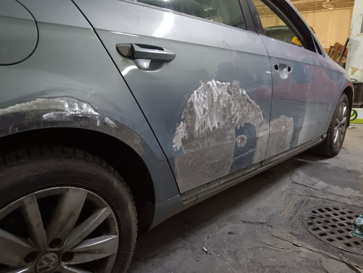 Volkswagen sedan gri-albastru cu aripa și ușa din spate chituite, în lucru, înainte de vopsire